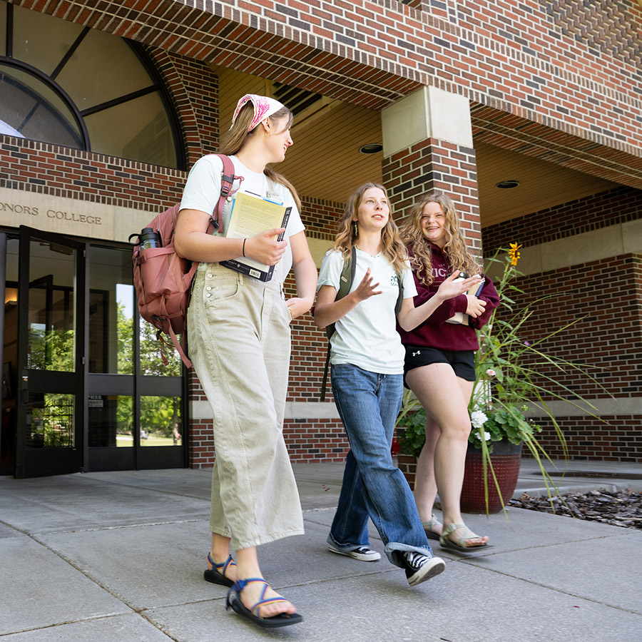 Three students talk as they walk out of the Davidson Honors College building at UM